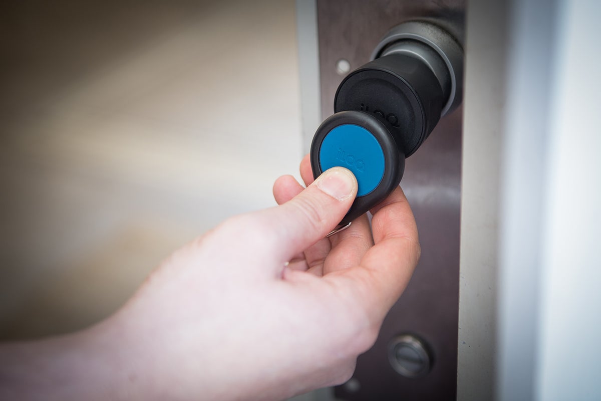 Eine Hand öffnet mit dem Smartkey eine Tür mit digitalem Türschloss.