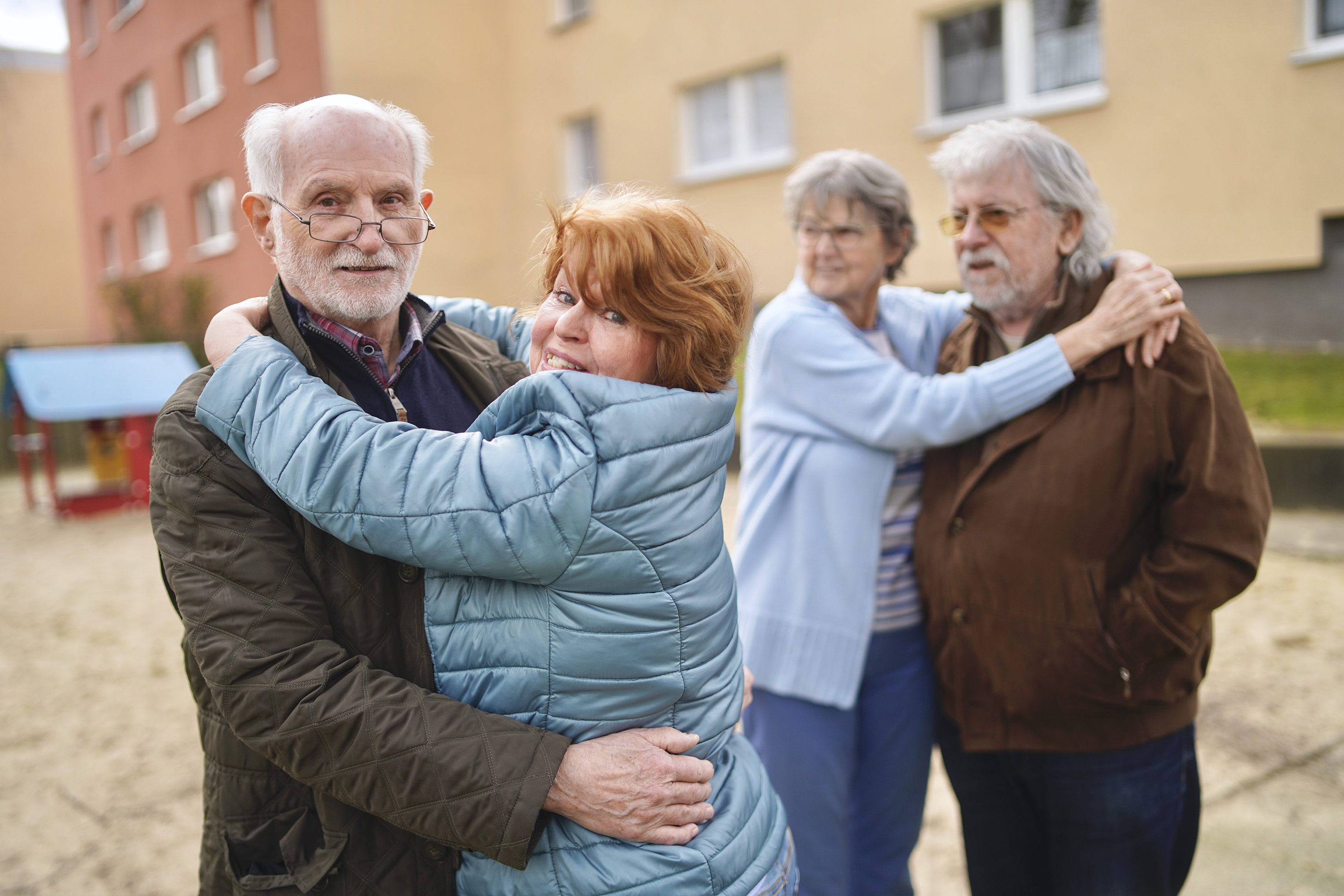 Paare umarmen sich im Freien vor einem Wohngebäude.