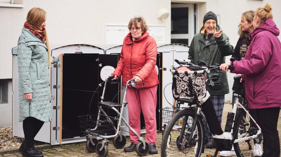 Frau schließt Schuppen, vier Personen unterhalten sich draußen. Frau schließt Schuppen, vier Personen unterhalten sich draußen.