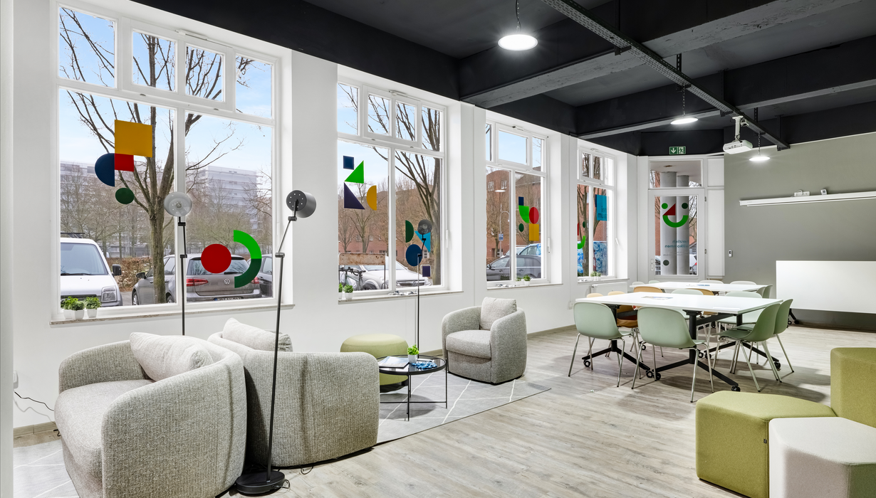 Raum mit bequemen Sitzmöglichkeiten, vielen Fenstern und einer grünen Wand auf der verschiedene Wörter stehen.