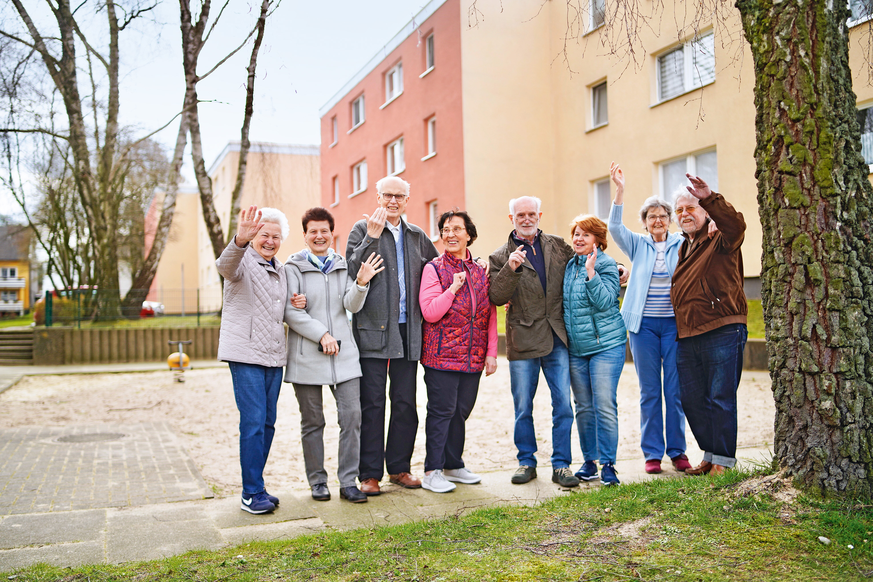Menschen winken vor einem Wohngebäude im Freien.