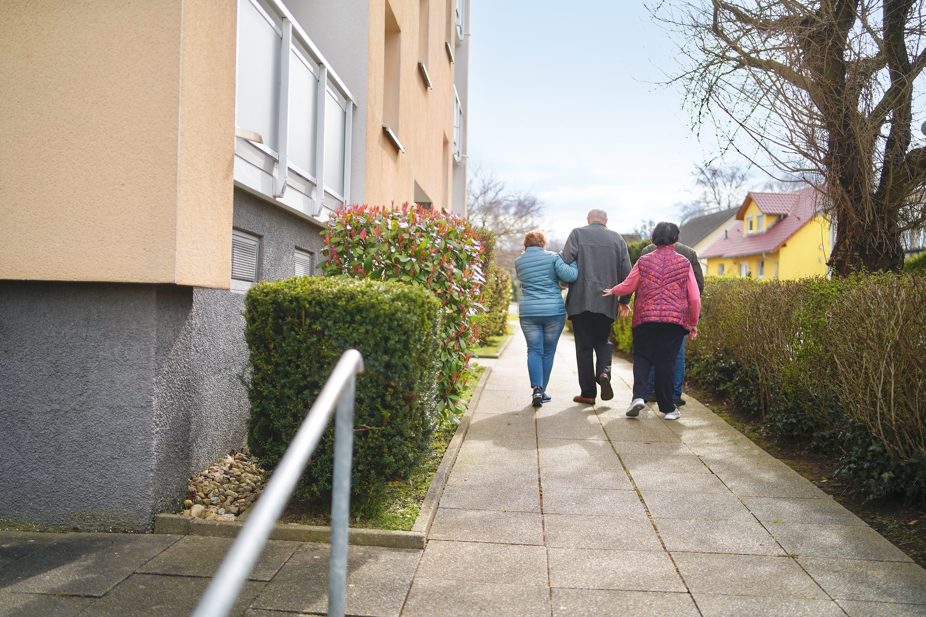 Vier Menschen spazieren auf einem Weg neben einem Wohngebäude.