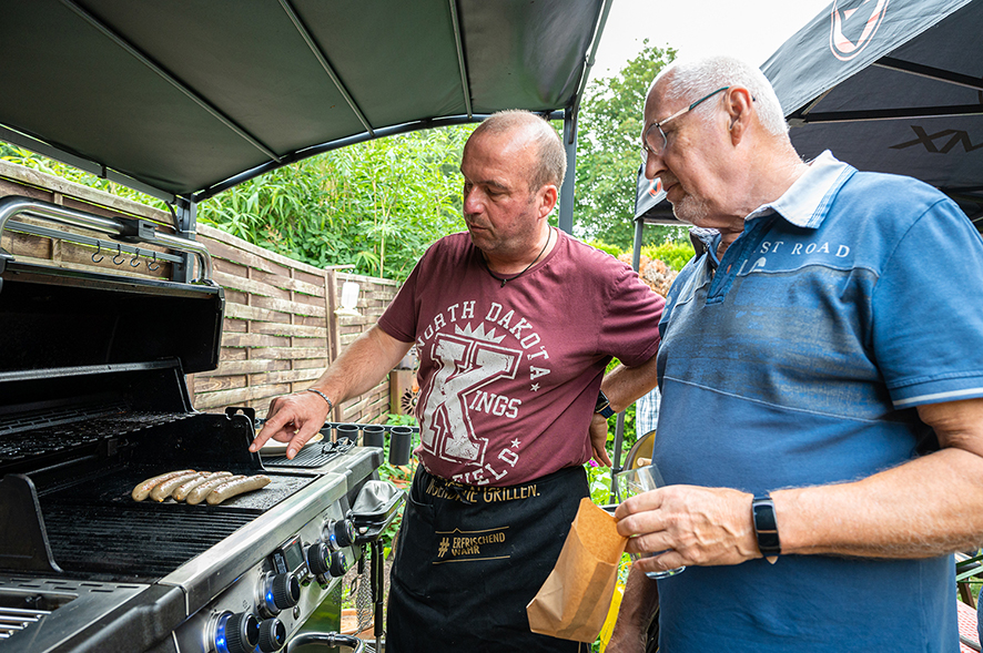 Zwei Männer grillen Würstchen im Garten.