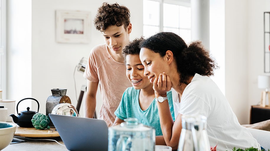 Gallery-Image-Familie-zusammen-in-der-kueche Familie guckt zusammen auf einen Laptop in der Küche
