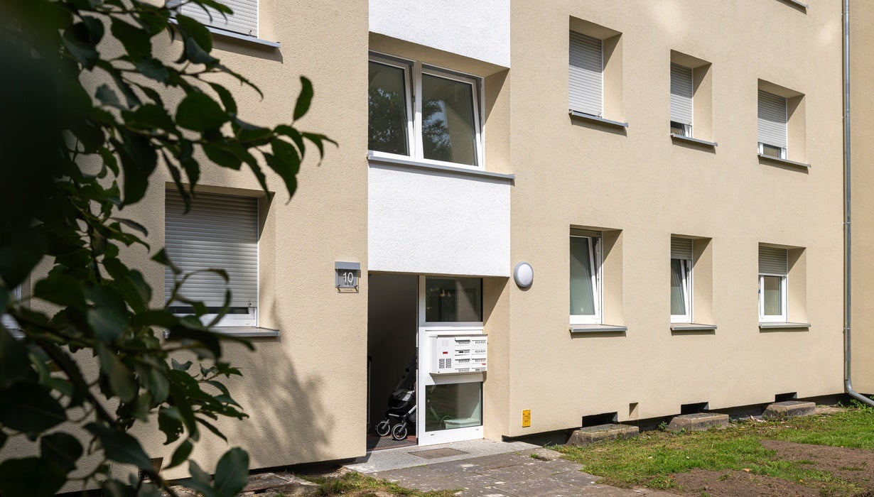 Die gelbe Fassade eines mehrstöckigen Wohngebäudes mit der Hausnummer 10 und einer geöffneten Eingangstür, hinter der ein Kinderwagen im Flur steht.