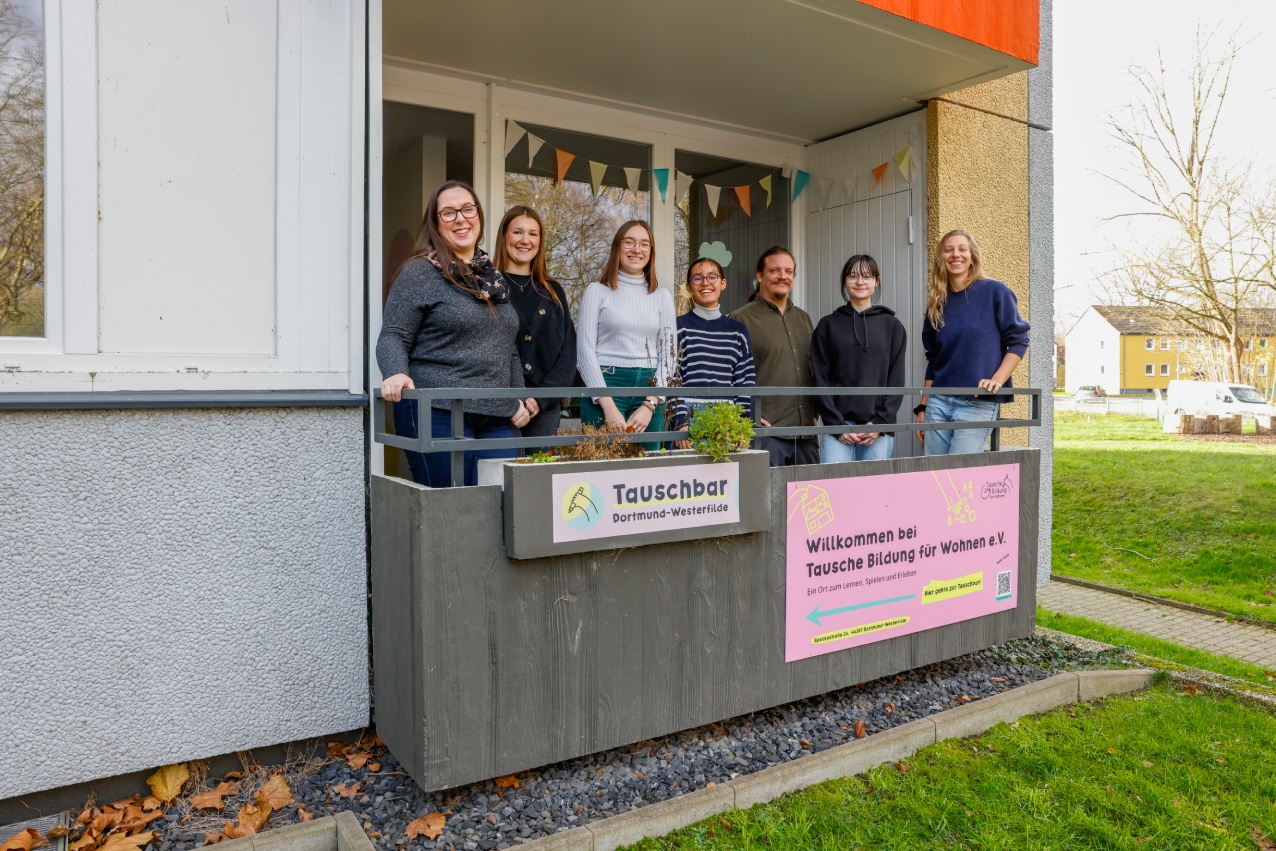 Gruppe von Personen steht auf Balkon mit Schild Tauschbar.