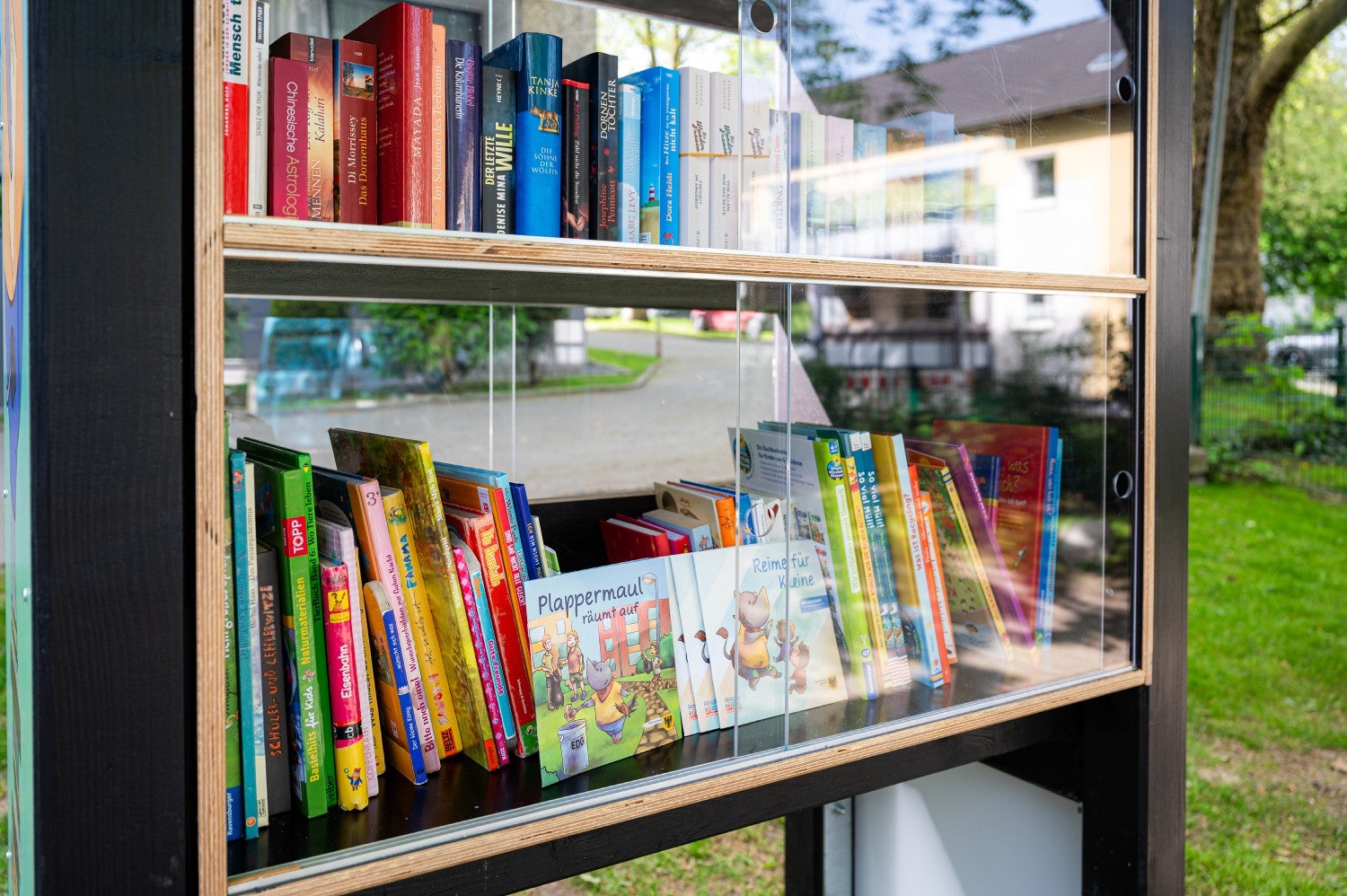 Aufnahme des Bücherschranks. Viele Bücher sind nebeneinander aufgereiht, geschützt von einer Glasschiebetür.