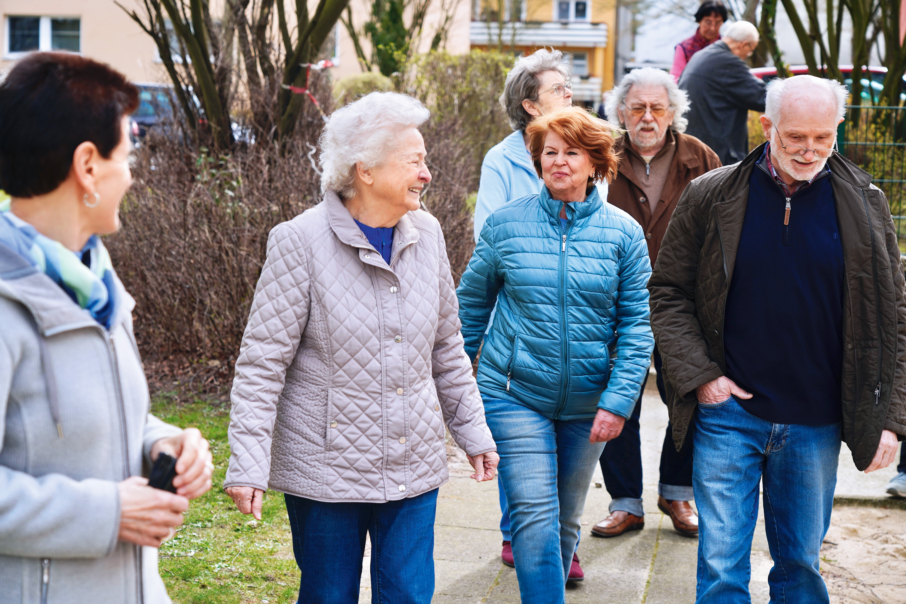 Seniorengruppe spaziert lachend in Wohngegend.