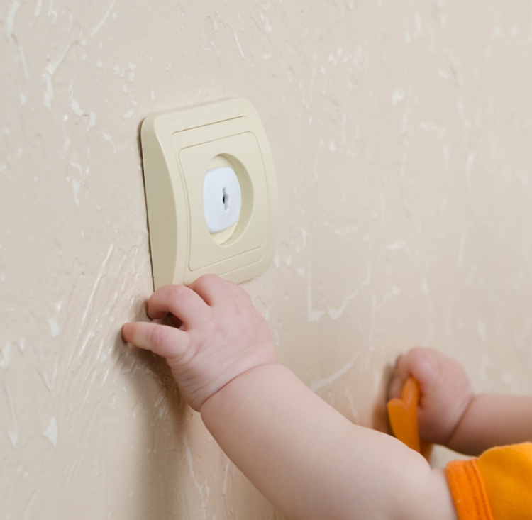 Ein Kleinkind fasst an eine gesicherte Steckdose. Ein Kleinkind fasst an eine gesicherte Steckdose.